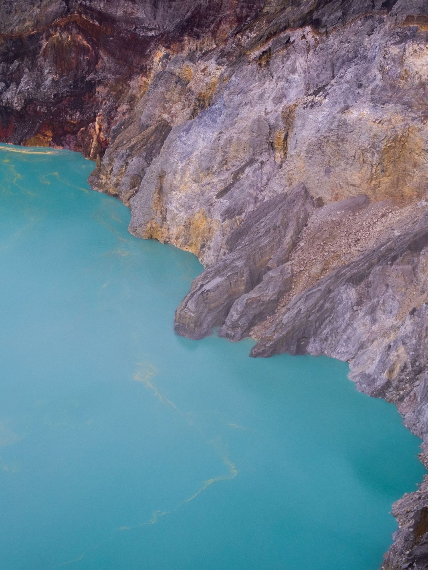 Turquoise glacial lake water meets rugged rocky cliff face in dramatic mountain landscape.
