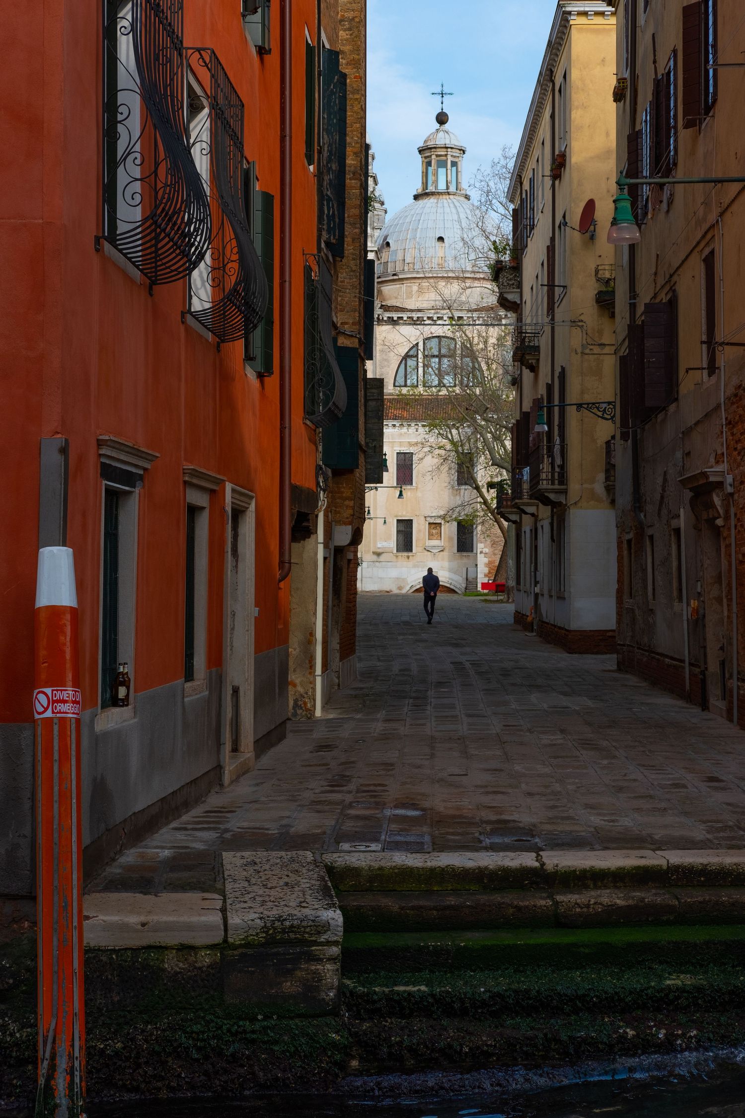 Narrow Venice alley with colorful orange walls leading to a domed church in the distance.