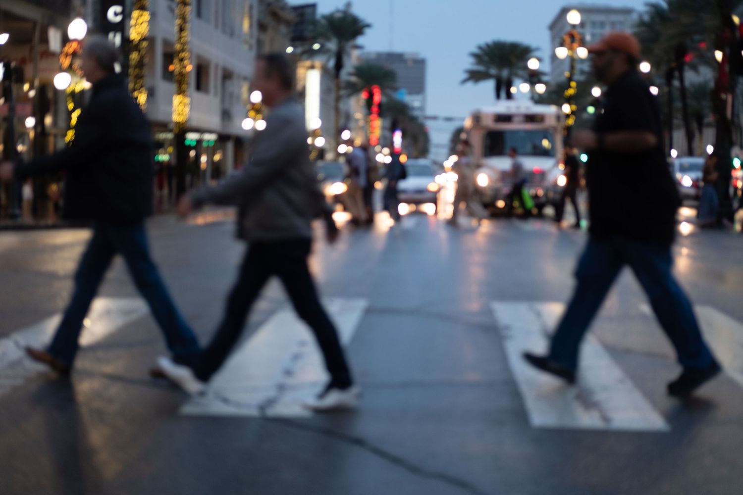 Silhouettes of pedestrians crossing a city street at night with blurred lights in the background.