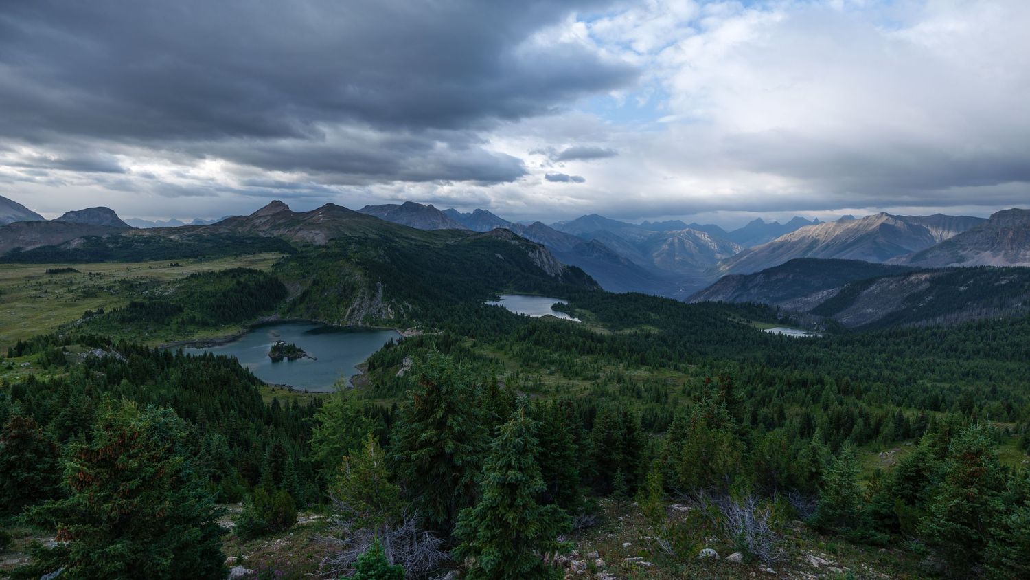 Dramatic panorama of mountain ranges and valleys under stormy skies and scattered sunlight.