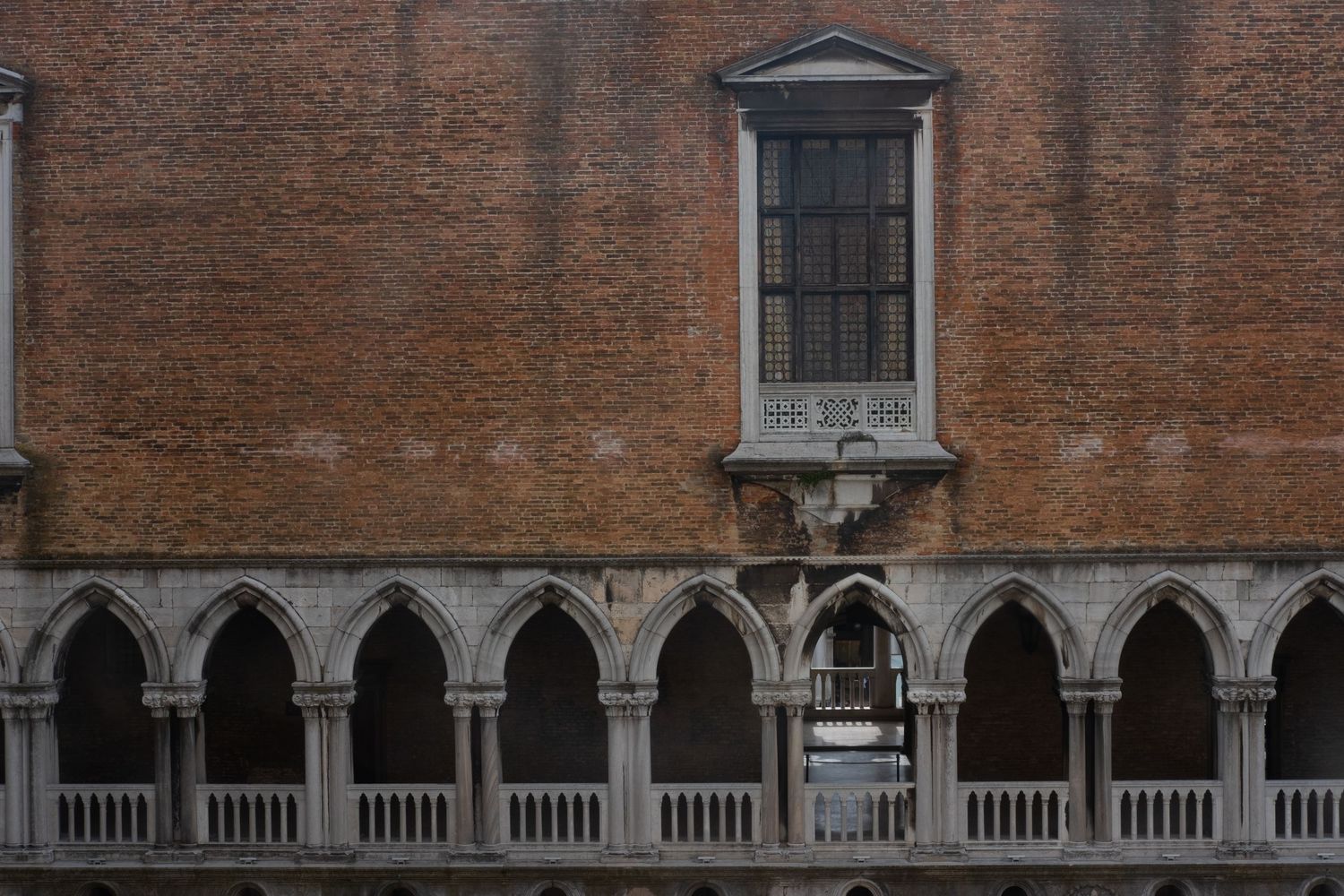 Brick wall with ornate arched colonnade and classical window detail in Venice.