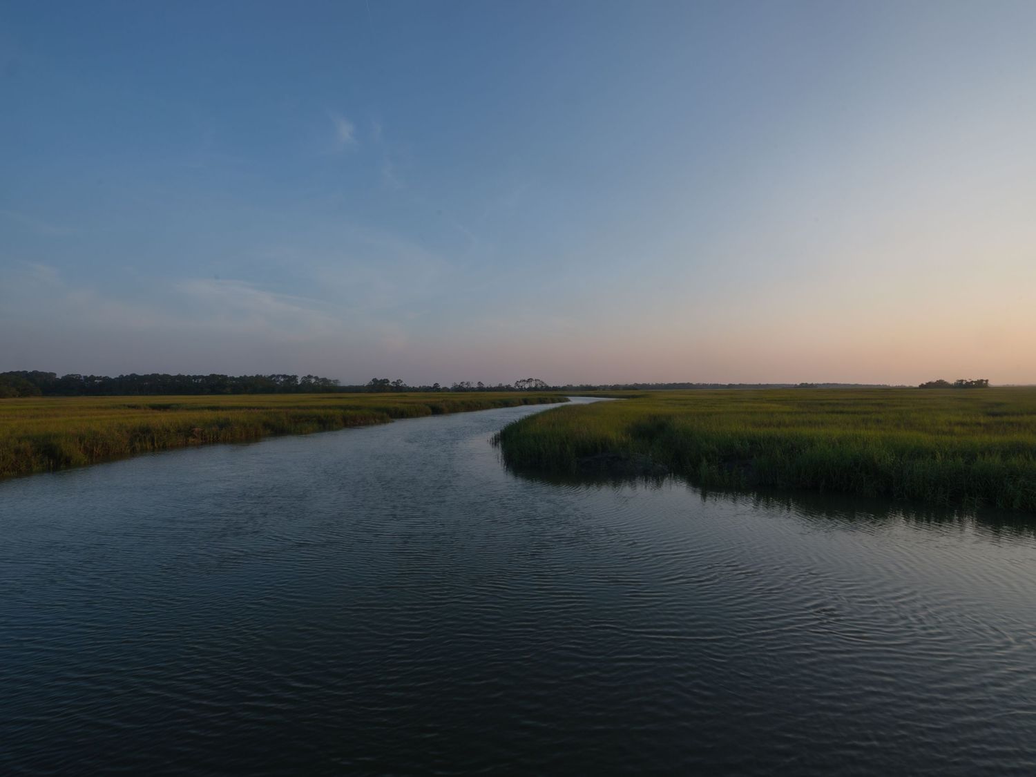 Serene panoramic view of a coastal marsh at sunset with calm waters reflecting the sky.