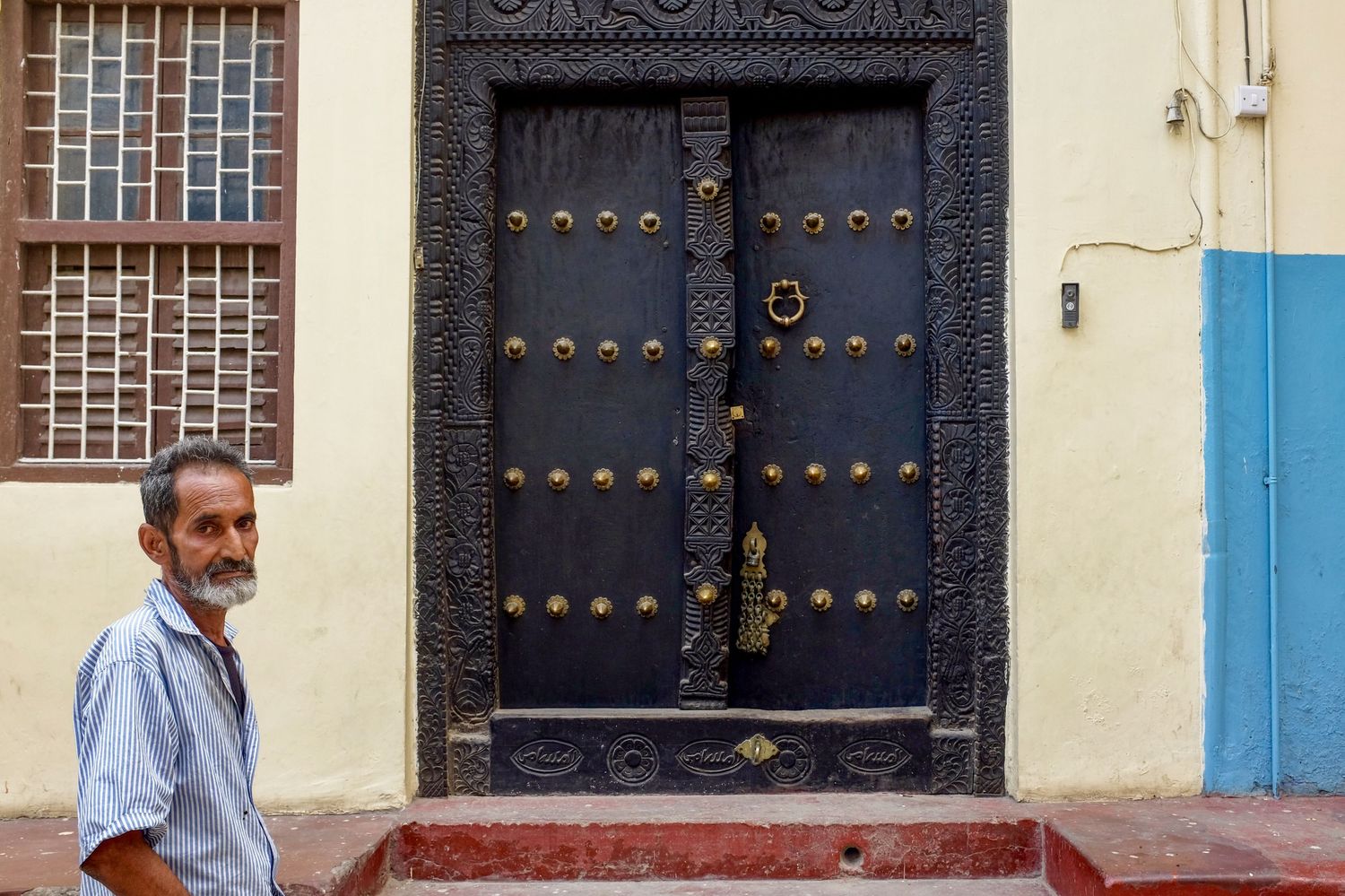 Row of ornate doors and windows on a yellow building facade with blue trim.