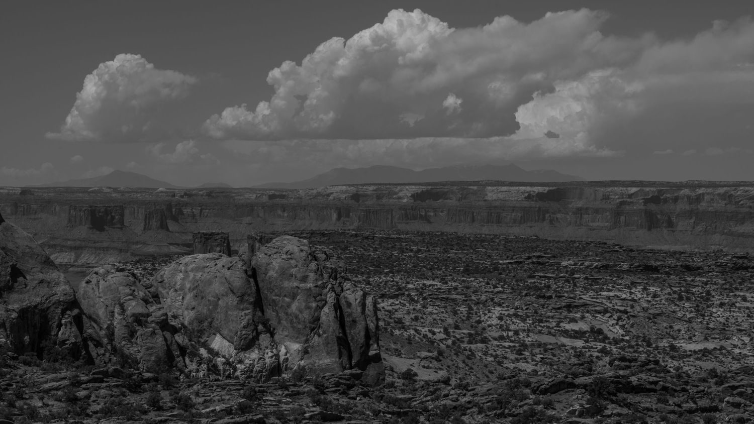 Expansive panoramic view of red rock formations in desert landscape under dramatic sky.