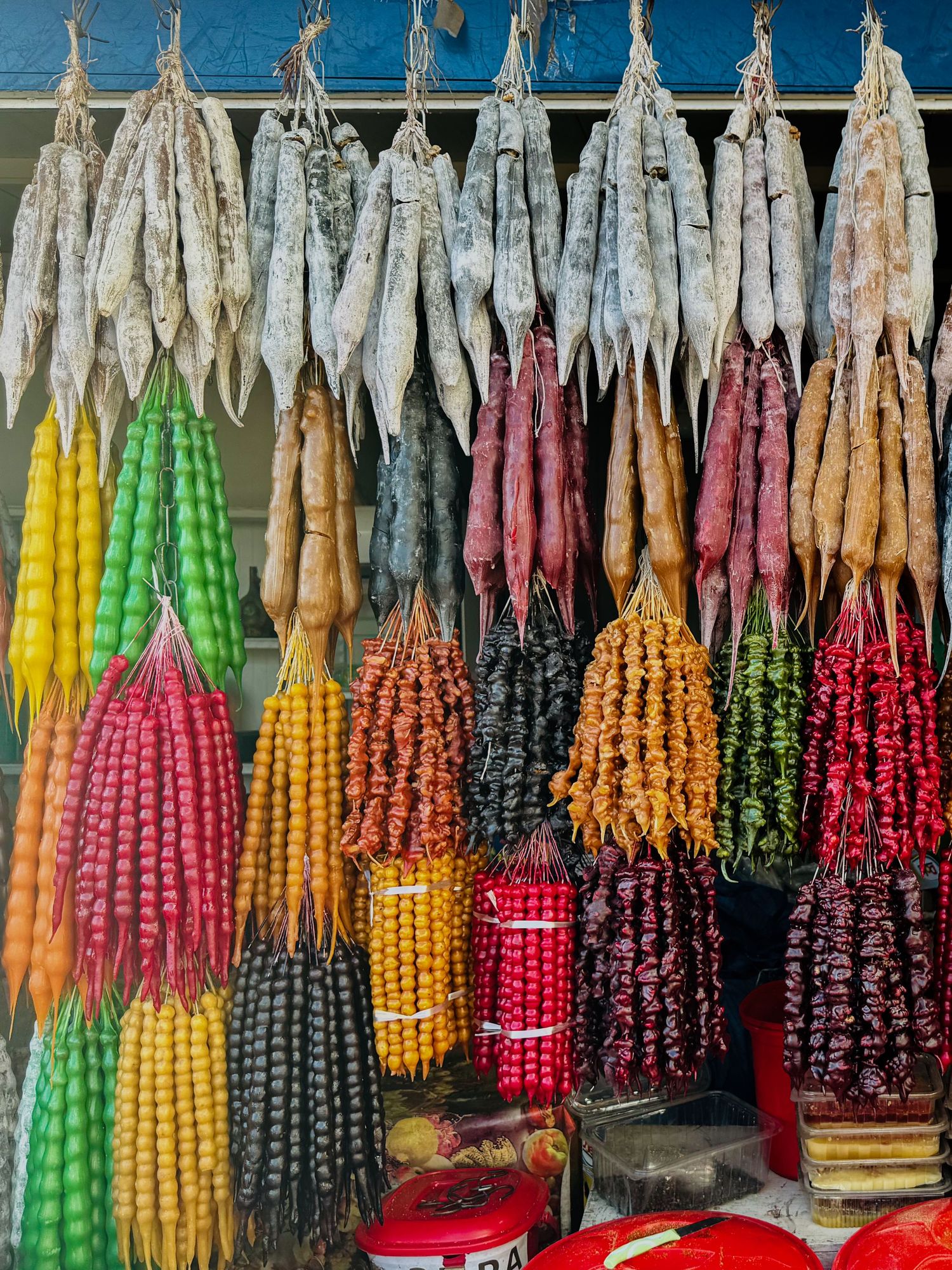 Colorful strings of dried chili peppers in various hues hanging at a market stall.