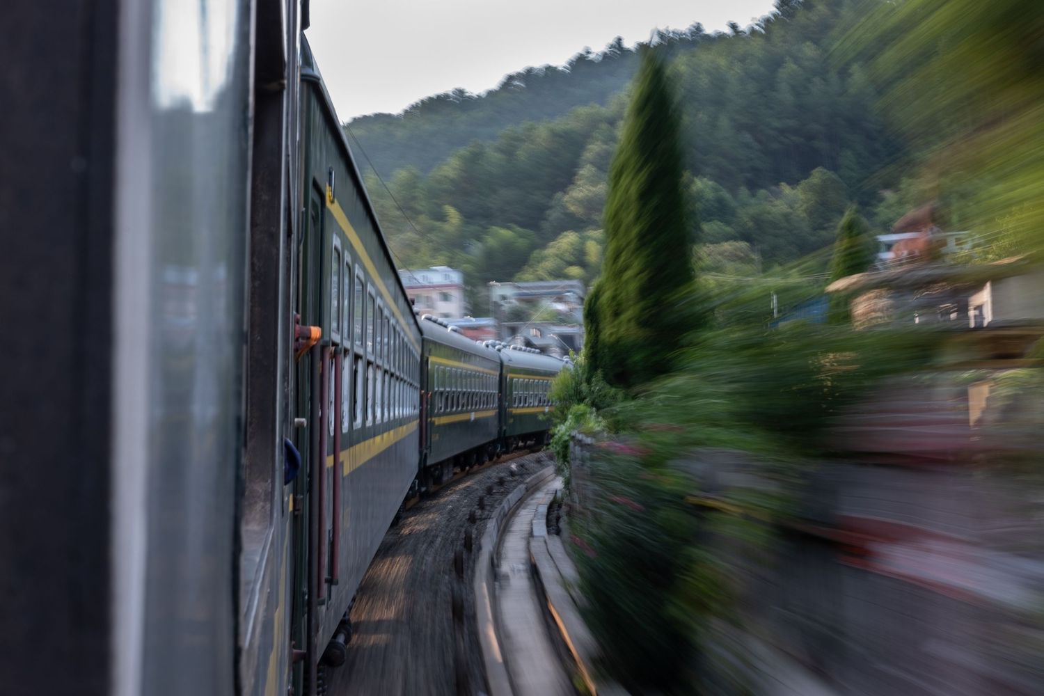 Motion-blurred view from a moving train window showing countryside scenery.
