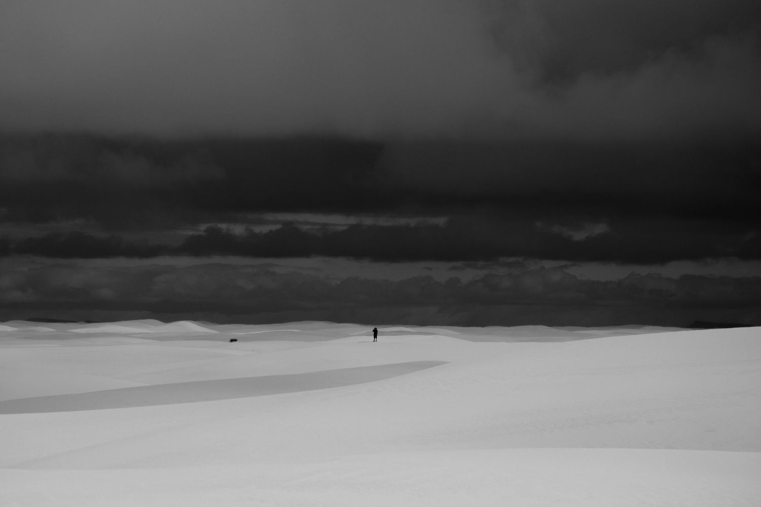A series of black and white minimalist landscape photographs showing rolling sand dunes under dramatic cloudy skies.