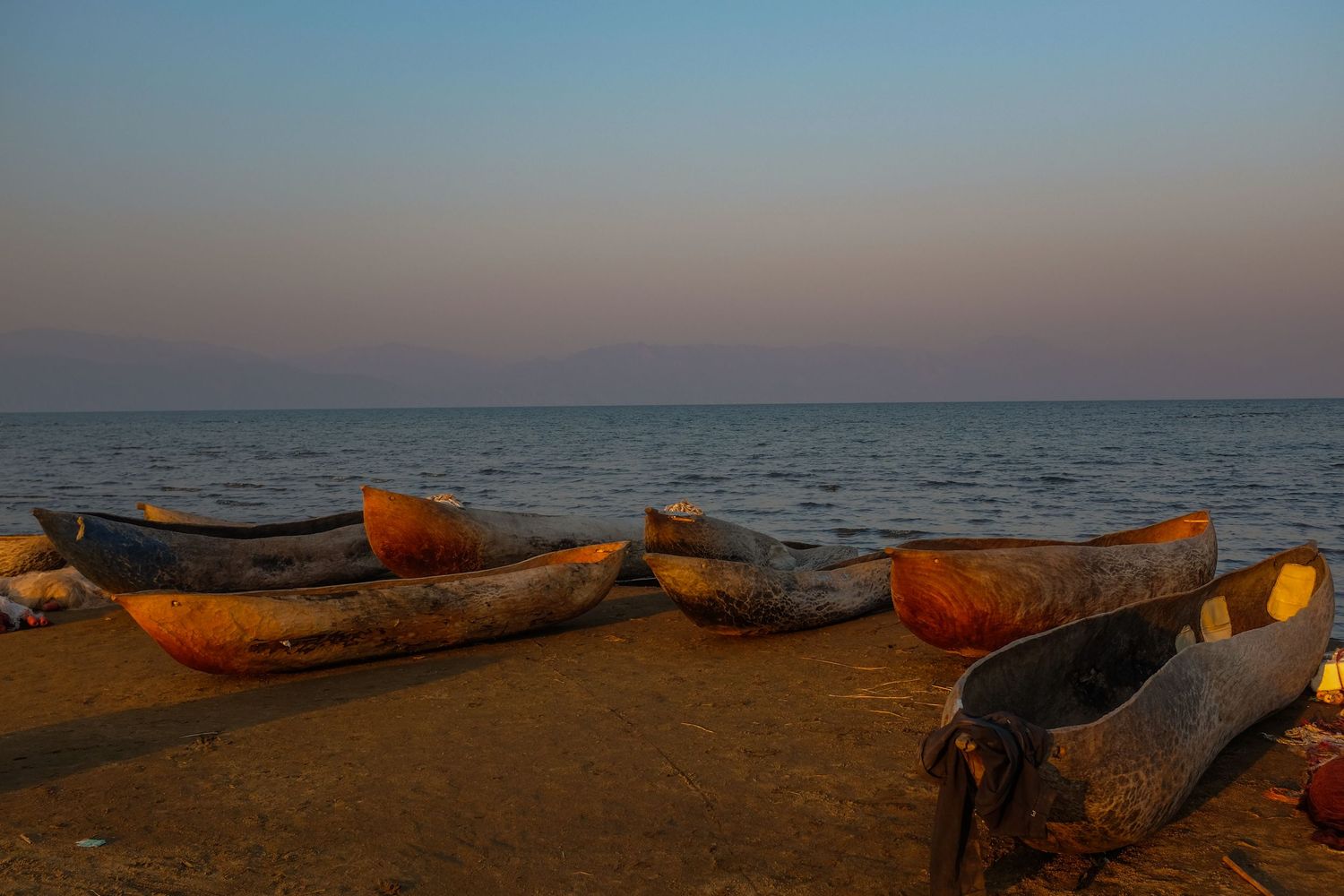 Wooden fishing boats rest on a beach at dusk with orange and purple sky reflections.