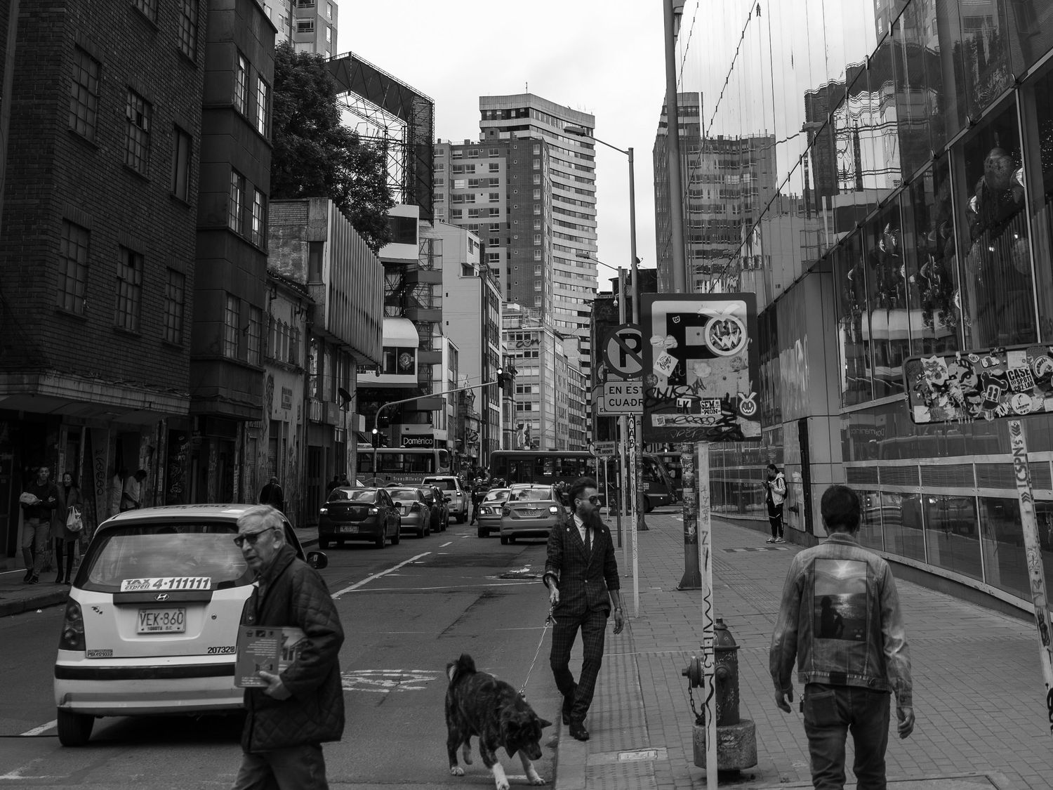 Urban street scene in black and white showing city buildings and pedestrians.