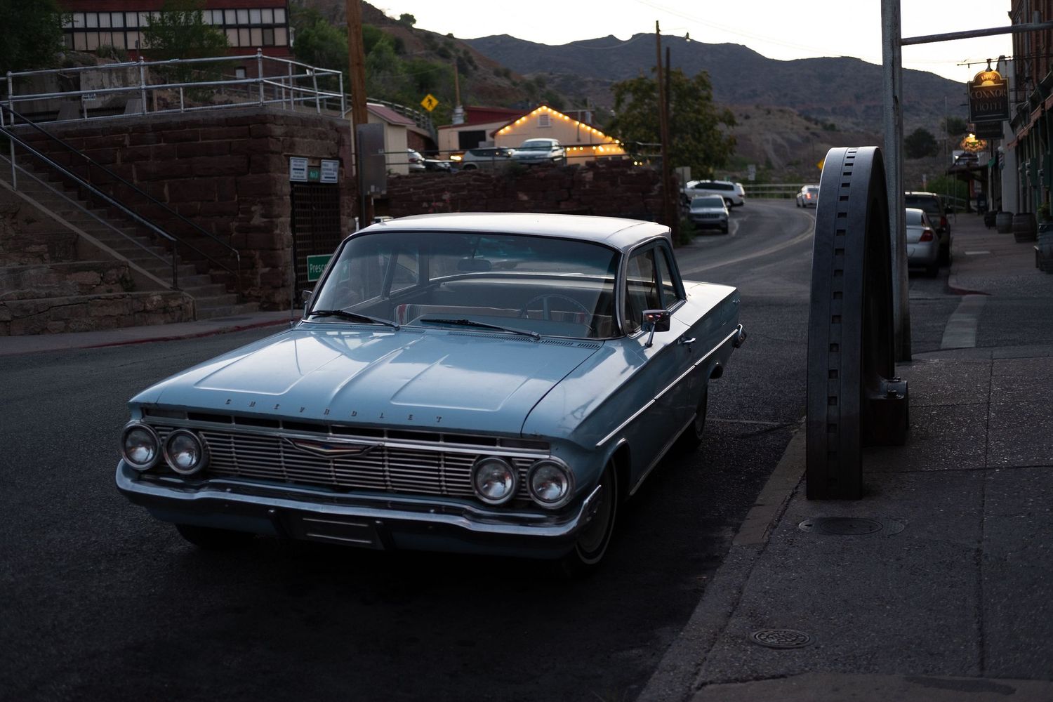 Classic vintage cars parked along a street at dusk with mountains in background.