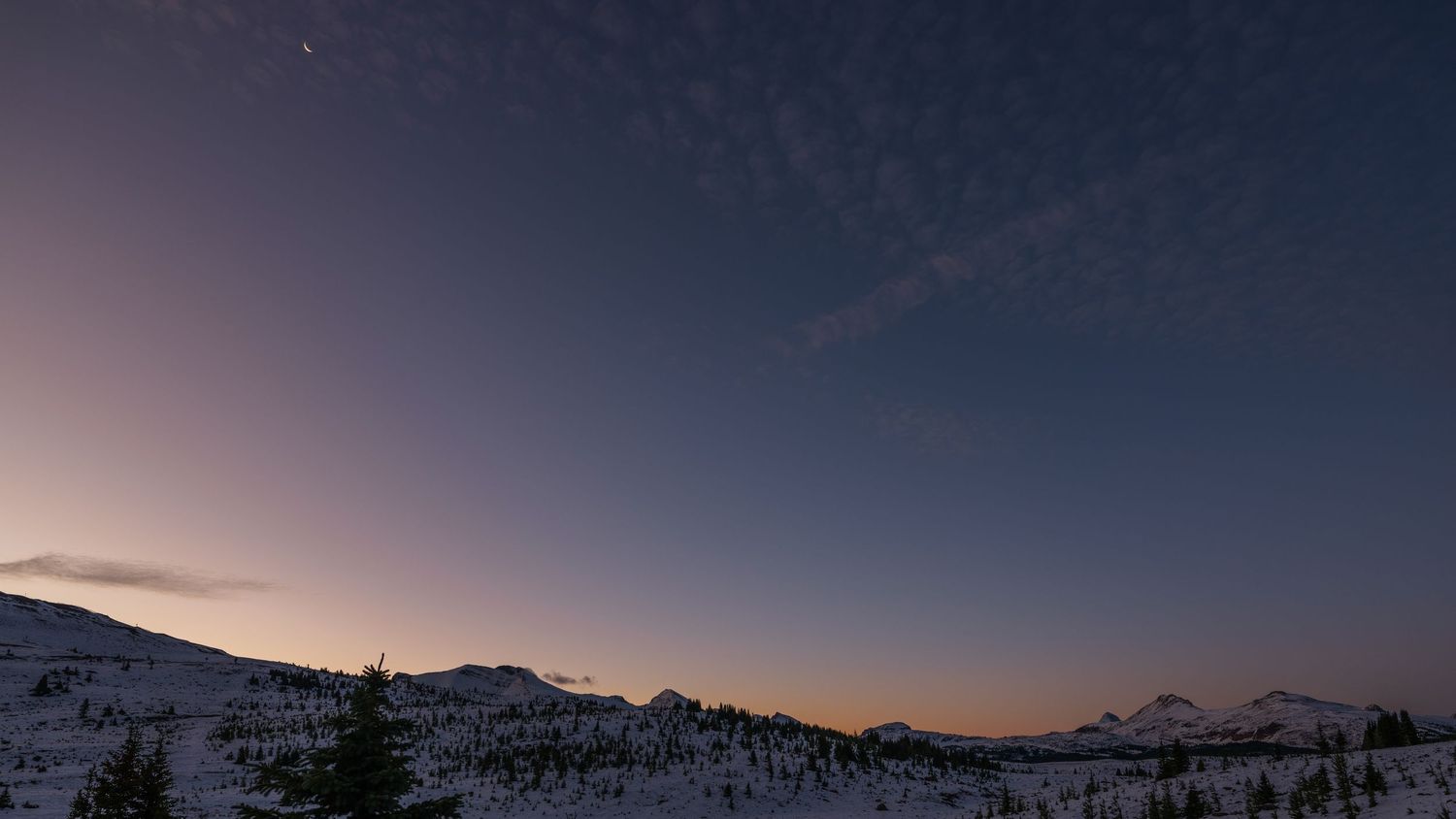 Snow-capped mountain range silhouetted against a purple twilight sky in winter.