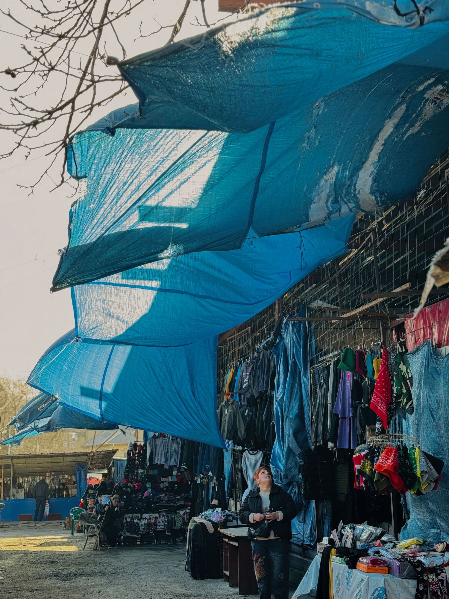 Market stalls with blue tarp coverings and clothing merchandise displayed.