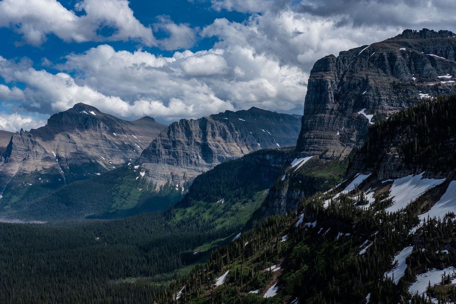 Dramatic mountain peaks with snow patches under cloudy skies in a rugged alpine landscape.