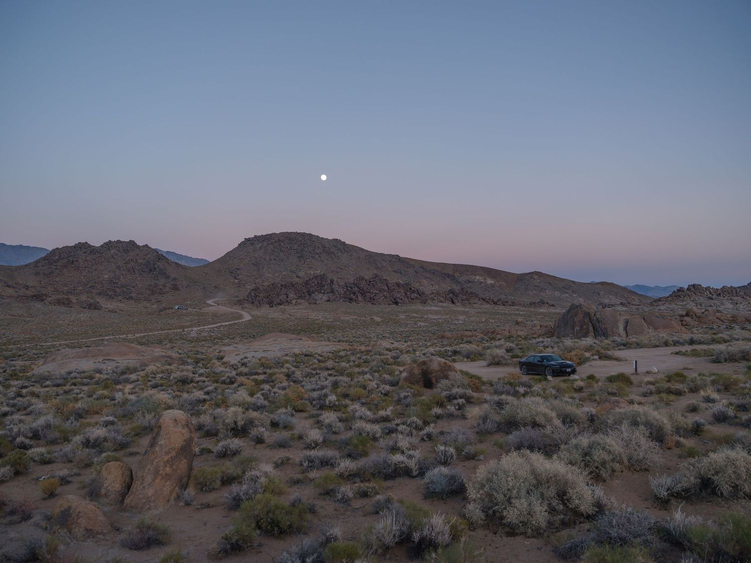Desert valley with scattered brush and rock formations at sunset.