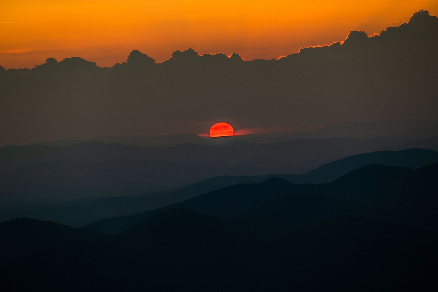 Dramatic orange sunset silhouetting mountain peaks against a darkening sky.