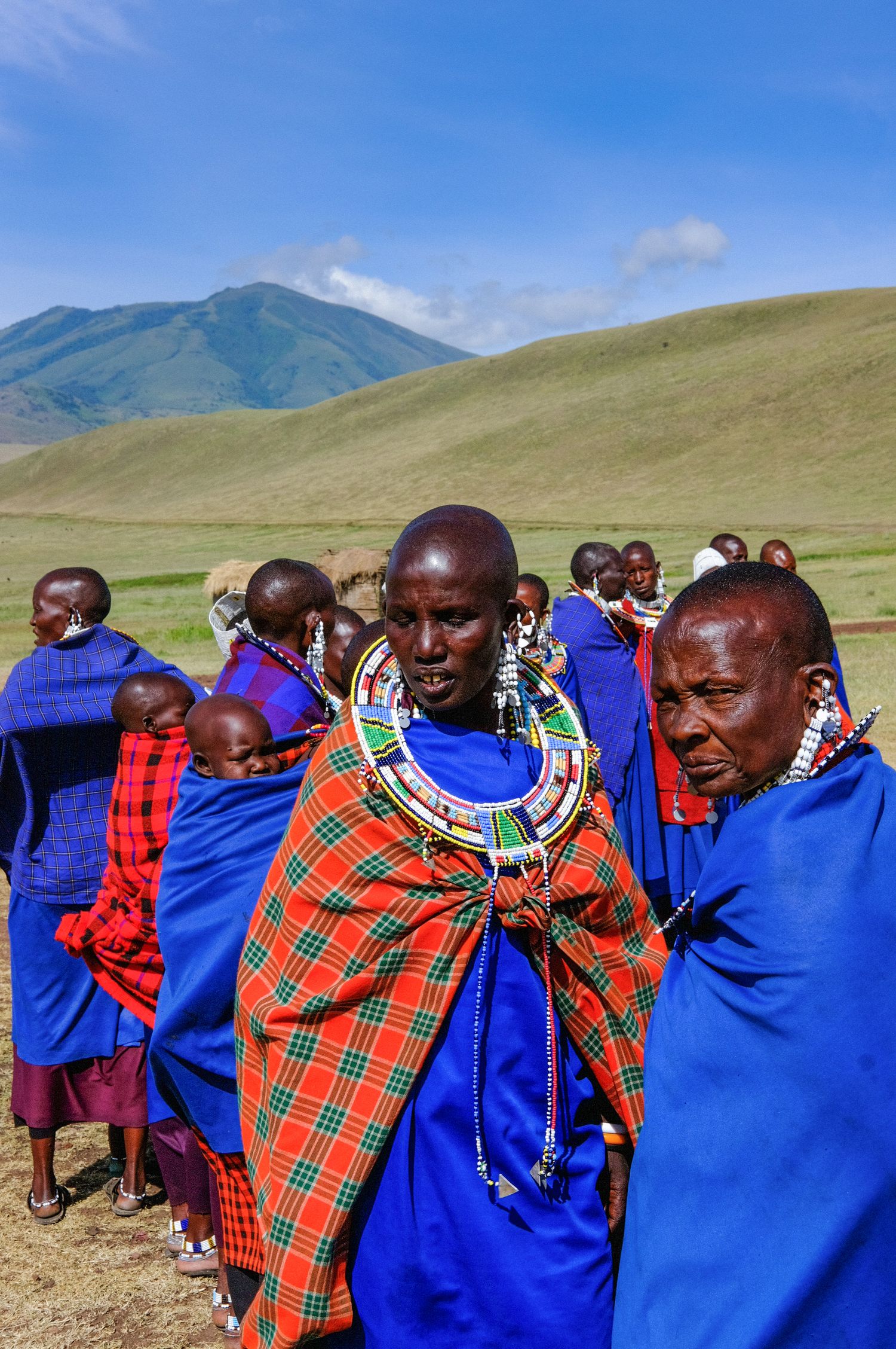 Maasai people in traditional blue and red clothing gathered in a scenic mountain landscape.