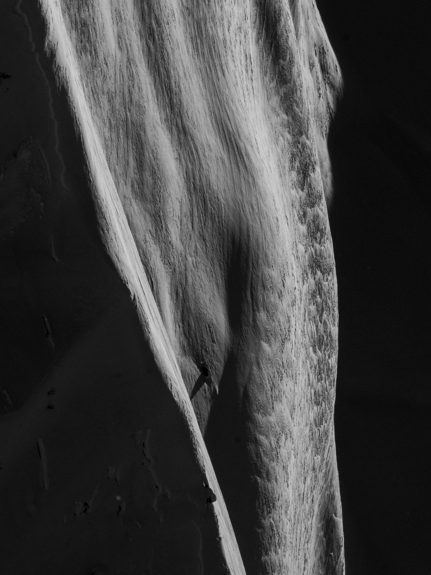 High contrast black and white photograph of a textured waterfall against dark background.