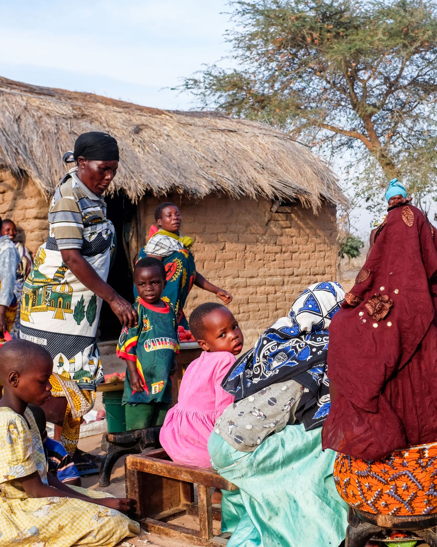 People gather outside traditional thatched-roof mud houses in a rural African village.
