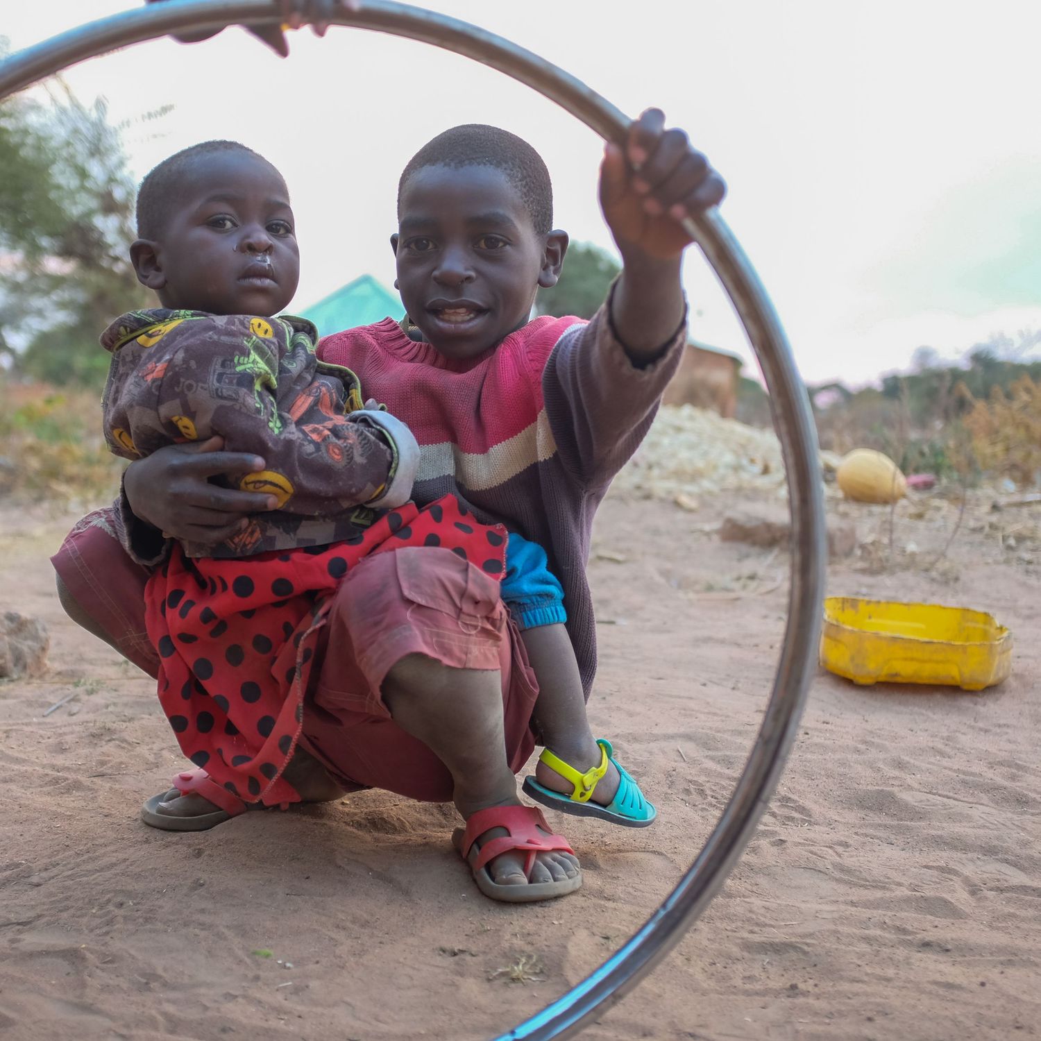 Children playing with a metal hoop on sandy ground.