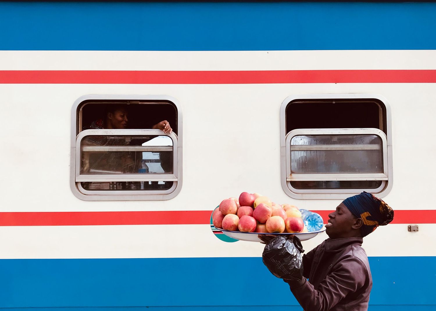 A person carrying red apples next to a blue and white striped train car.