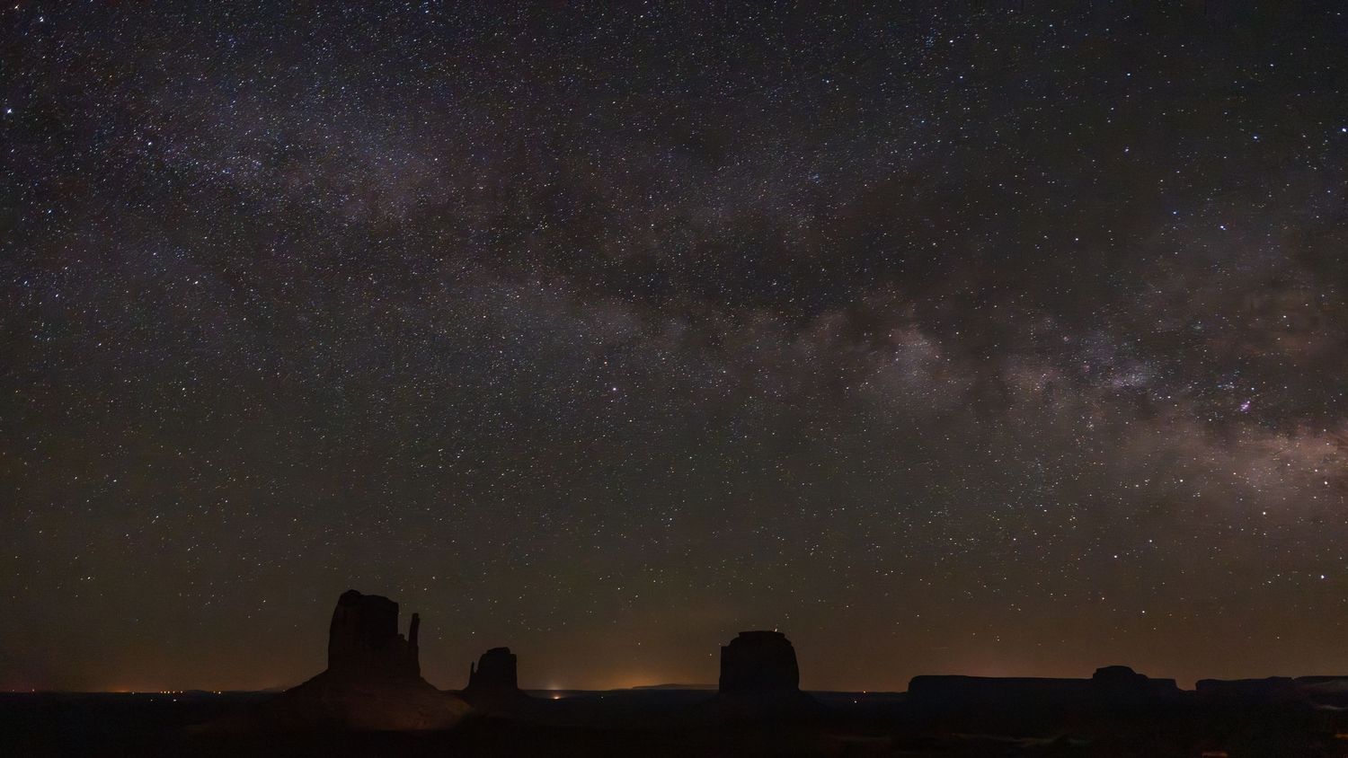 Panoramic view of Monument Valley silhouetted against a starry night sky.