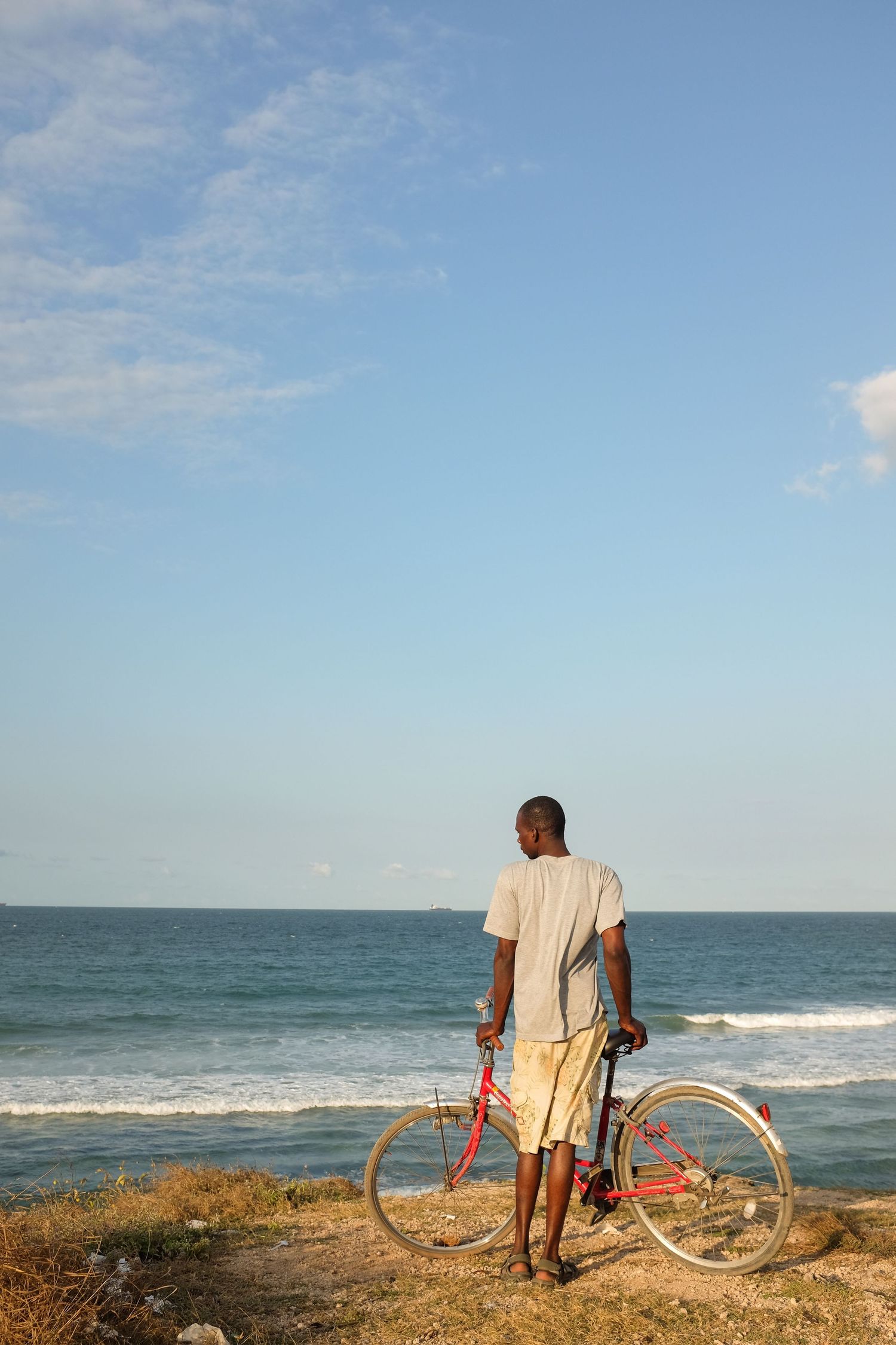 Person with bicycle looking out over ocean waves on a sandy beach.