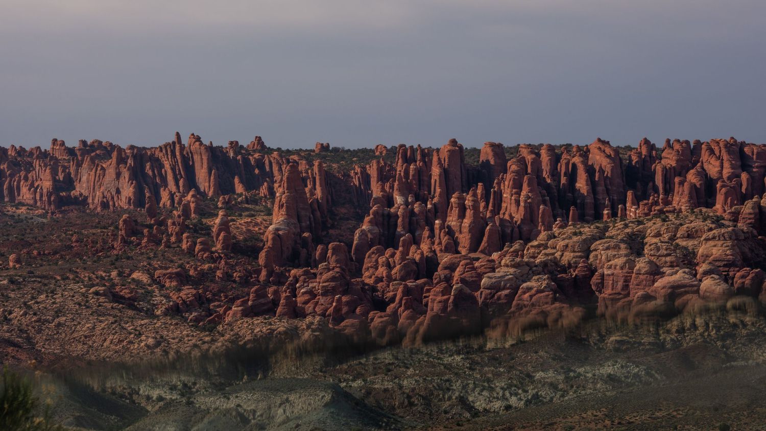 Panoramic vista of red sandstone cliffs stretching across a desert landscape at sunset.