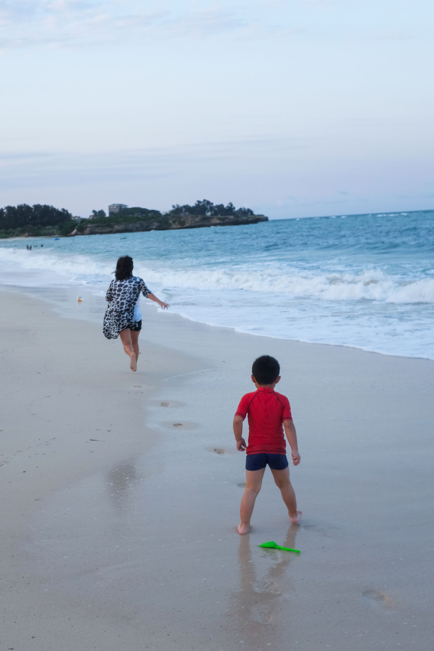 People playing and running along the shoreline as waves crash on a tropical beach.