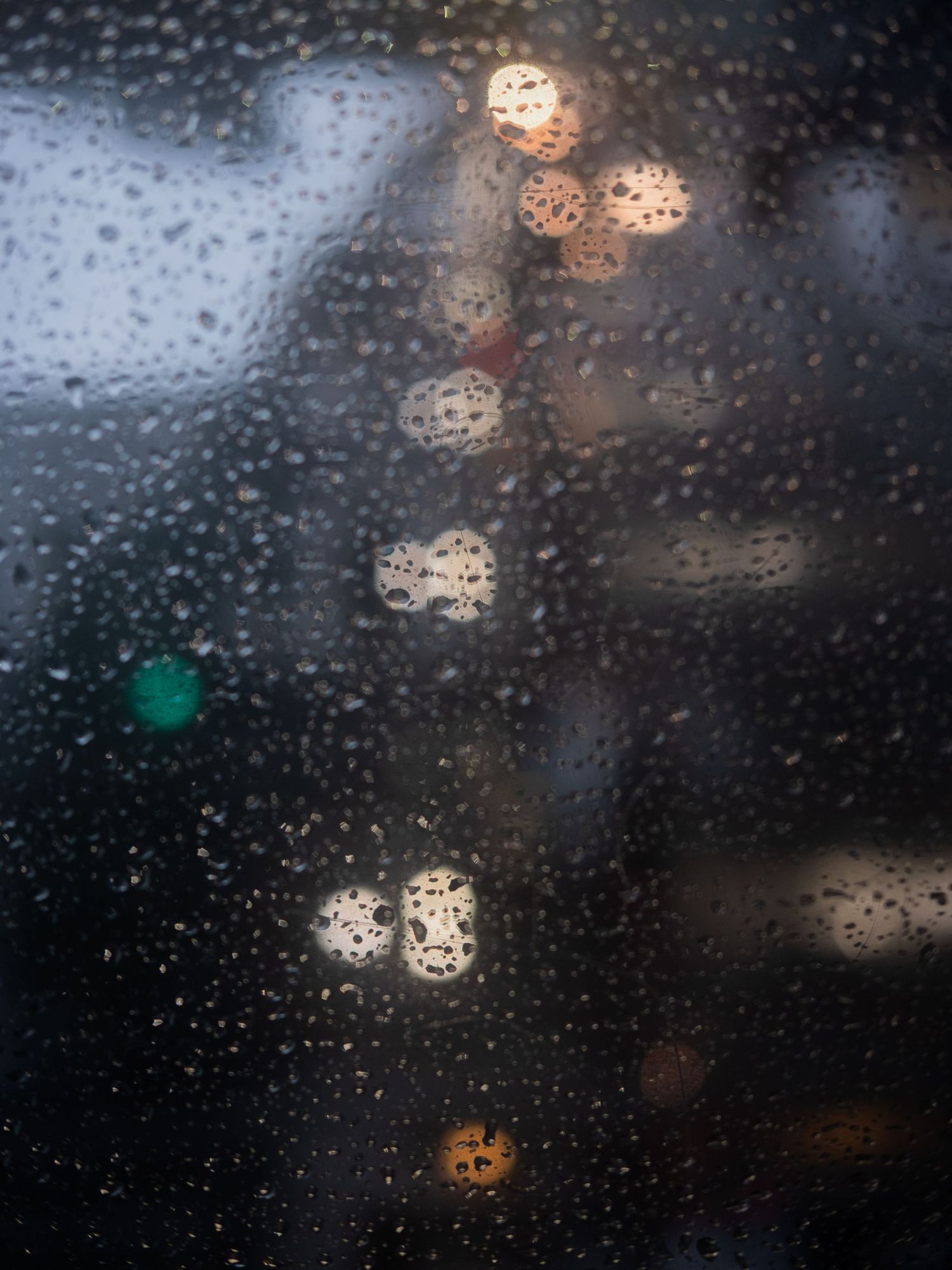 Raindrops on glass window with blurred city lights creating bokeh effect at night.