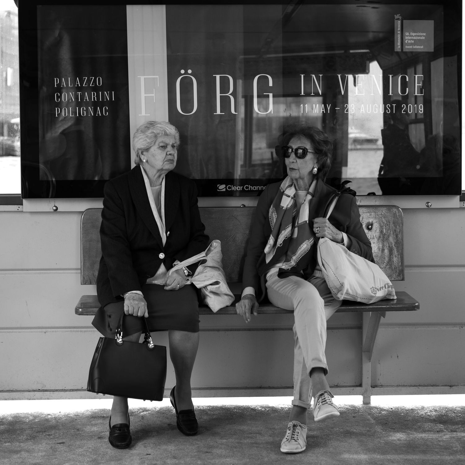 People sitting on bench outside storefront in black and white photograph.