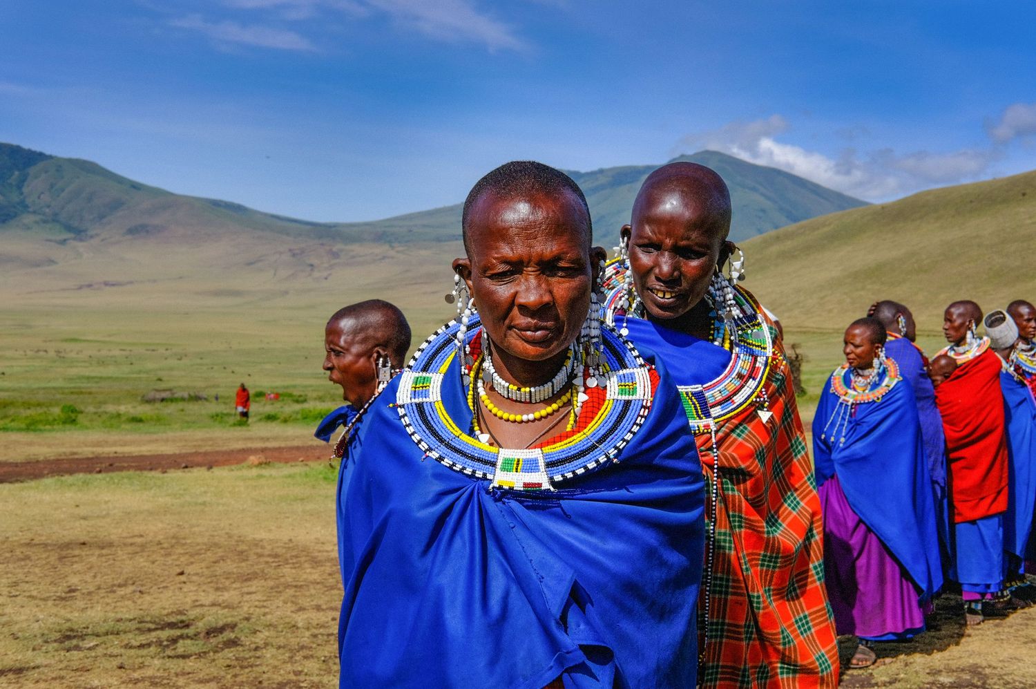 Group wearing traditional Maasai clothing with blue and red garments against mountain backdrop.