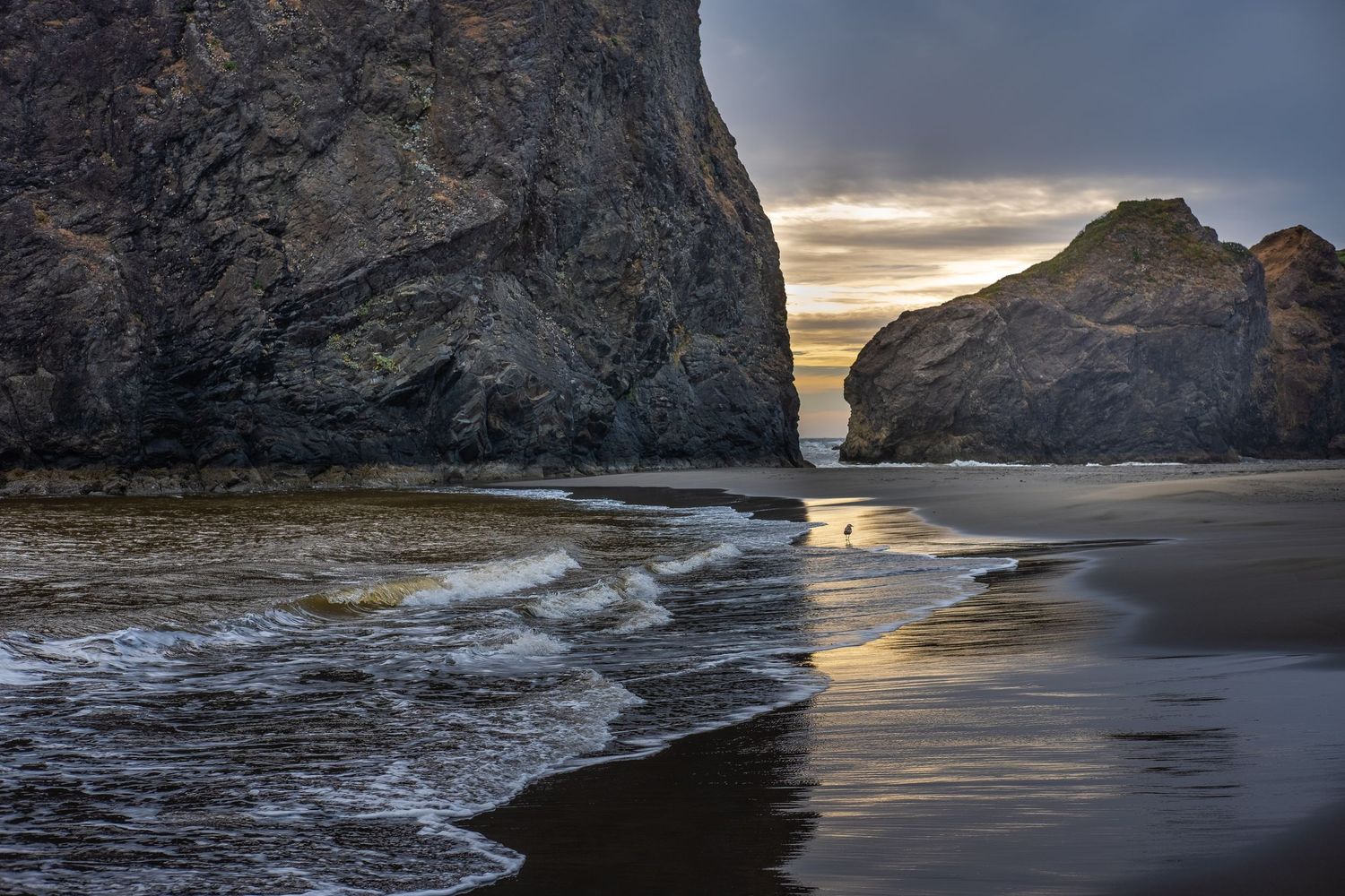 Rocky coastal cliffs and sea stacks at sunset with dramatic ocean waves crashing against the shore.
