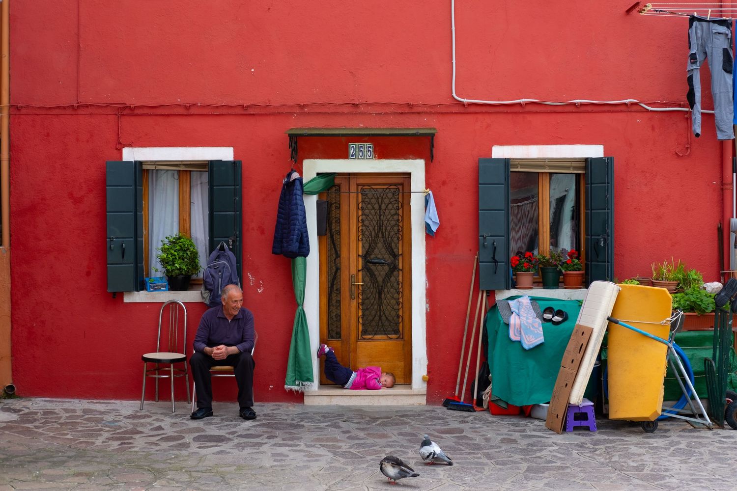 Vibrant red house exterior with green shutters and colorful household items outside.