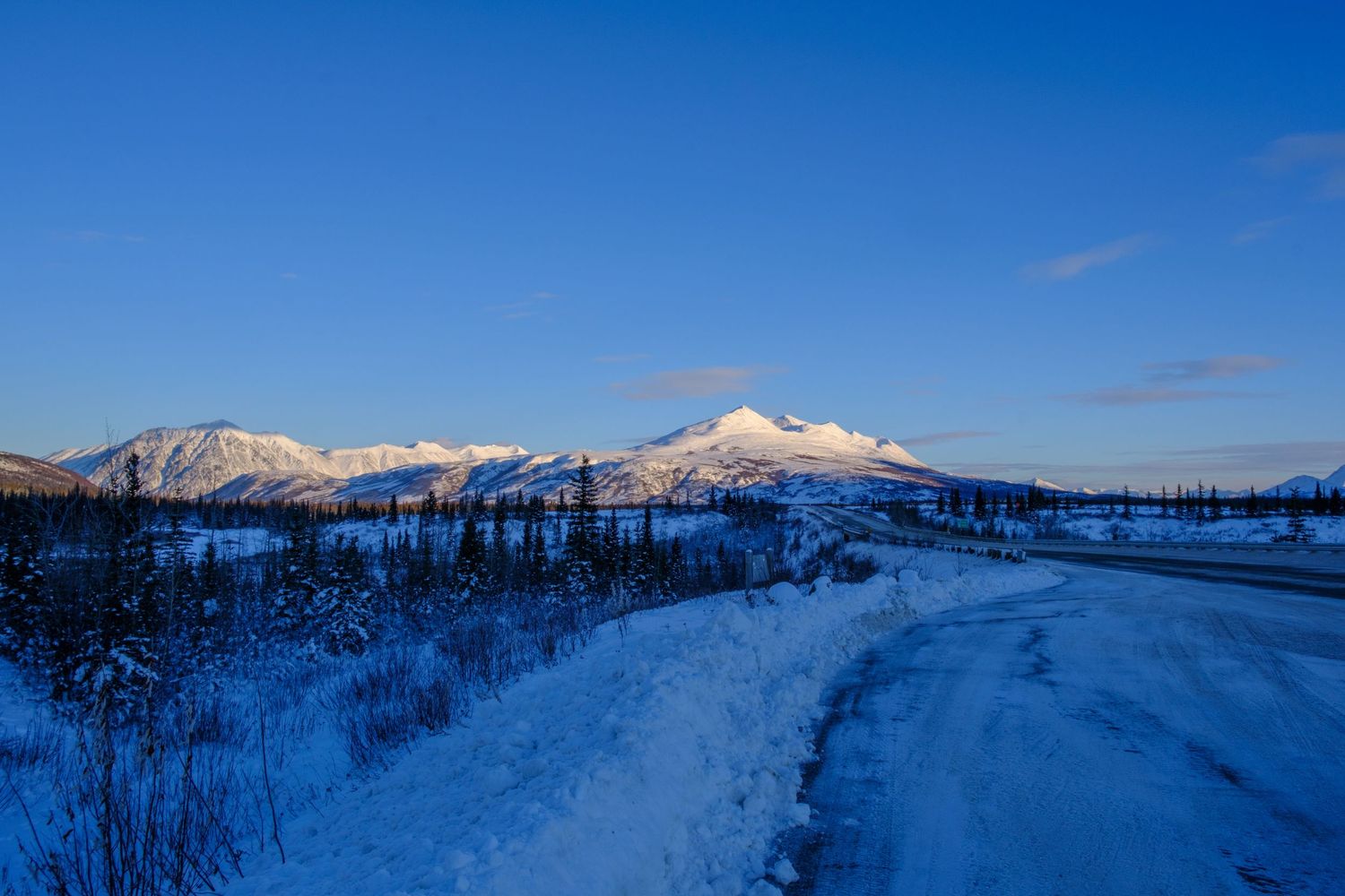 Snow-covered mountain landscape with evergreen trees under bright blue winter sky.