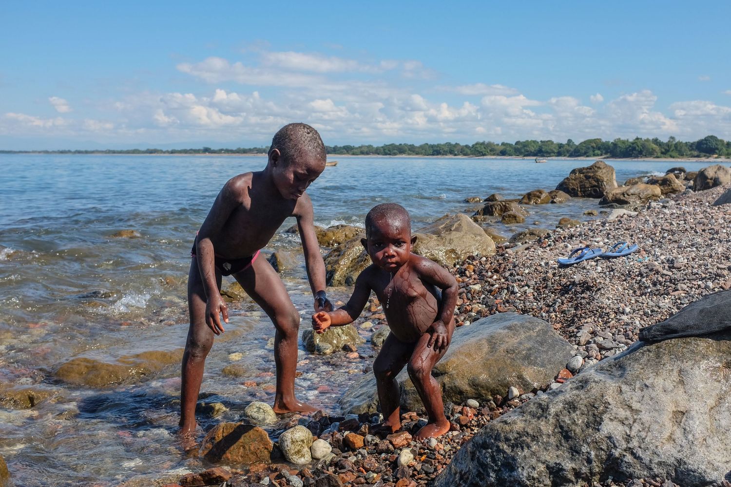 People collecting shells and exploring the rocky shoreline at low tide on a sunny beach day.