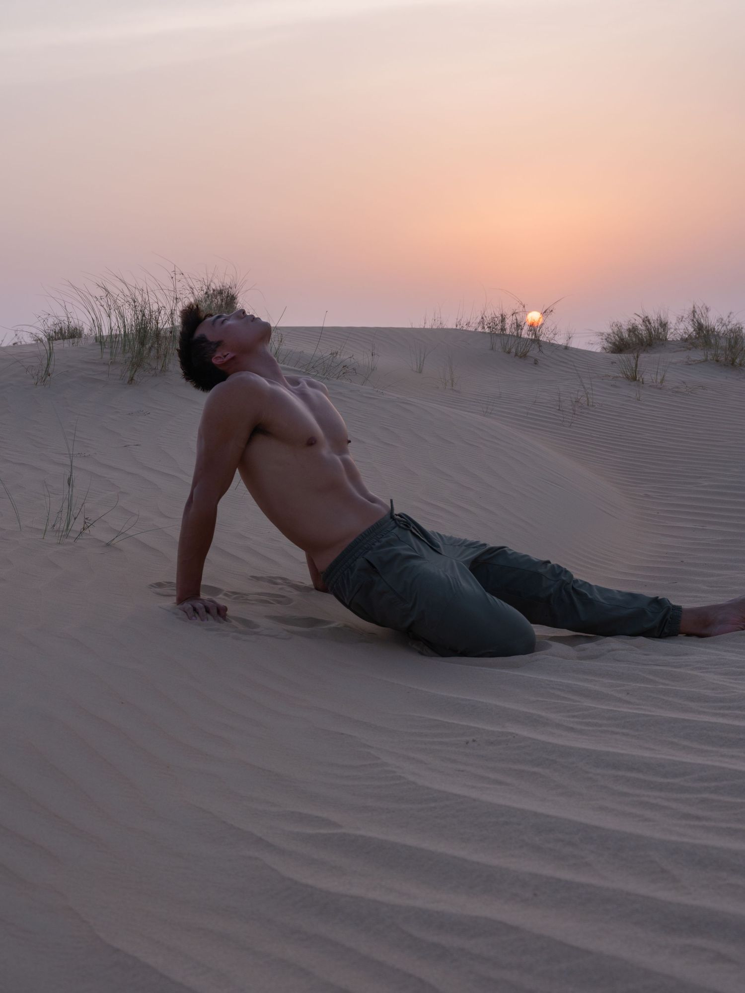 A person slides down a sandy desert dune at sunset, creating ripples in the golden sand.
