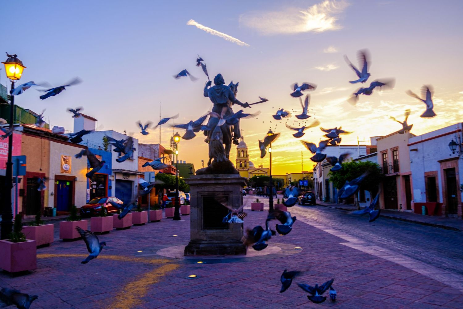 Pigeons take flight at dusk against colorful buildings in a charming colonial town street.