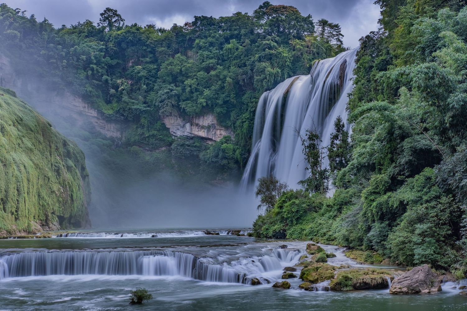 Majestic waterfall cascading through lush forest landscape in misty conditions.