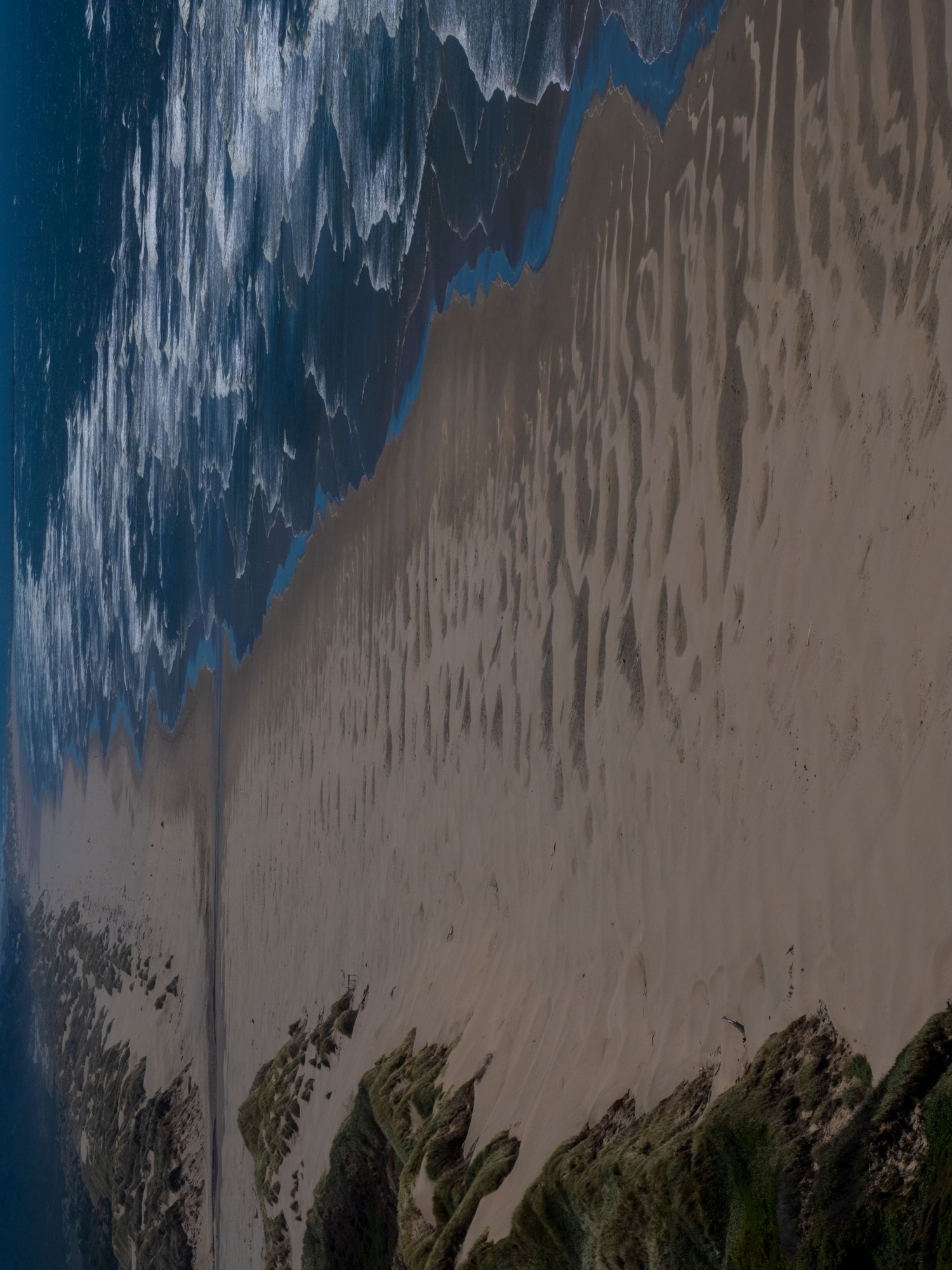 Abstract diagonal composition of ocean waves meeting sandy beach from aerial perspective.