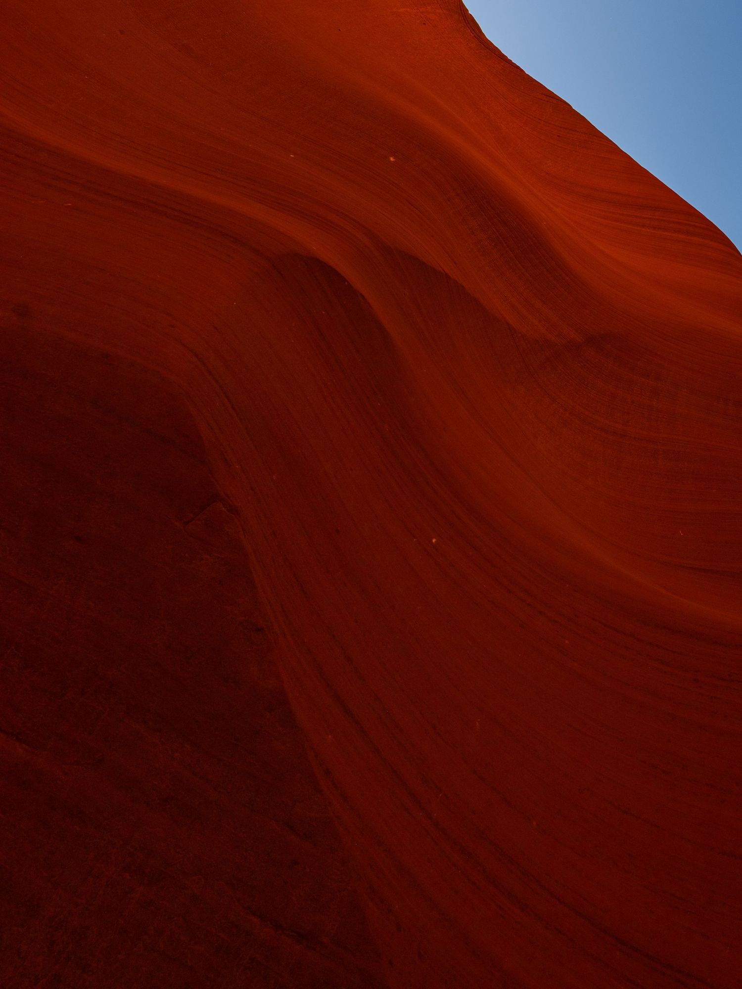 Smooth curved red sandstone formation against bright blue sky.