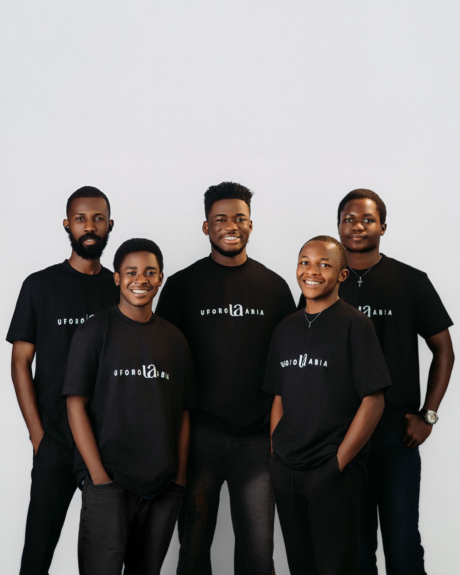 Group photo of five men in coordinated black t-shirts standing together against white backdrop.