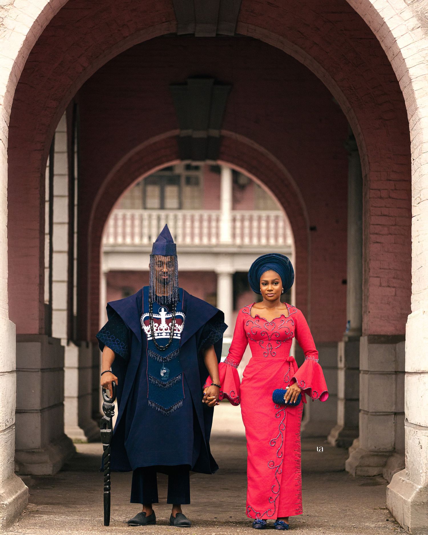 Wedding party poses under arched brick columns in navy and red formal attire.