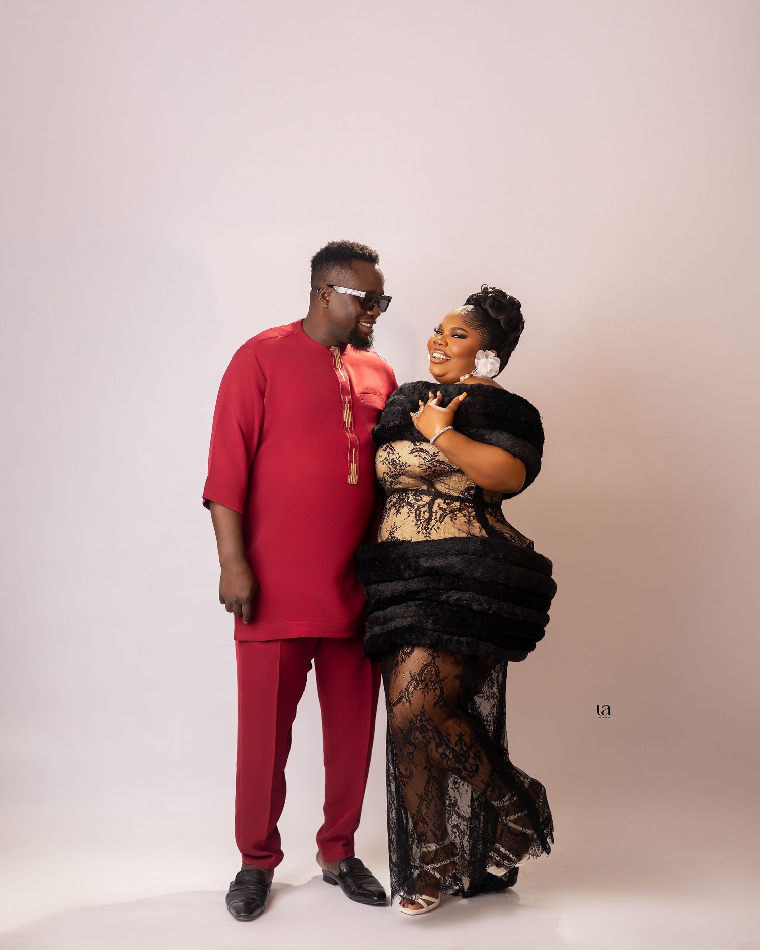 Romantic couple poses in studio wearing contrasting red and black formal outfits against neutral backdrop.