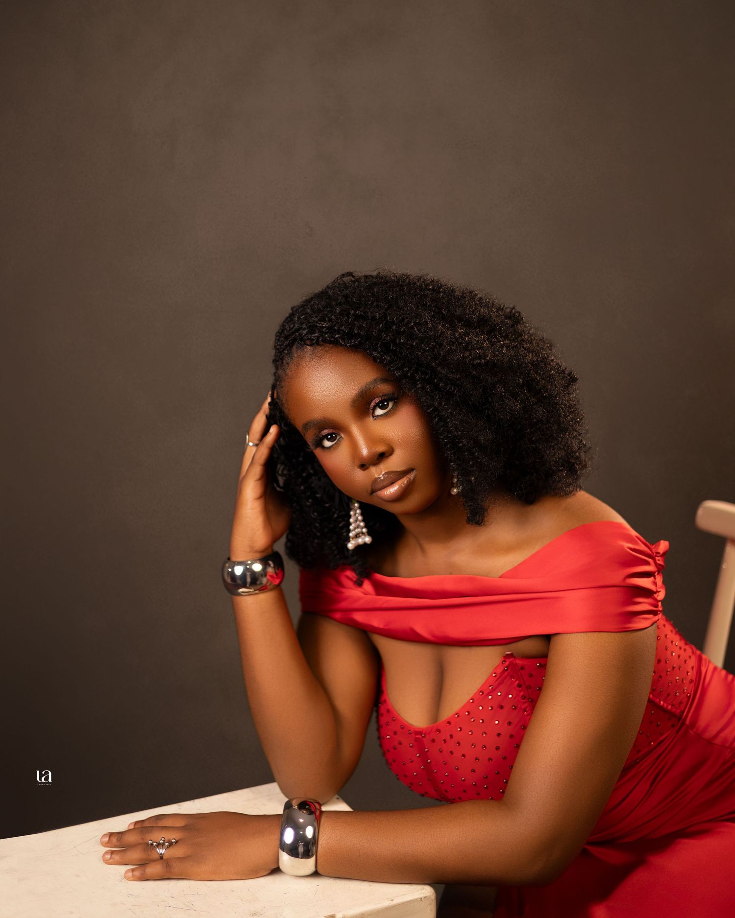 A glamorous portrait in a red dress with statement jewelry against a neutral background.
