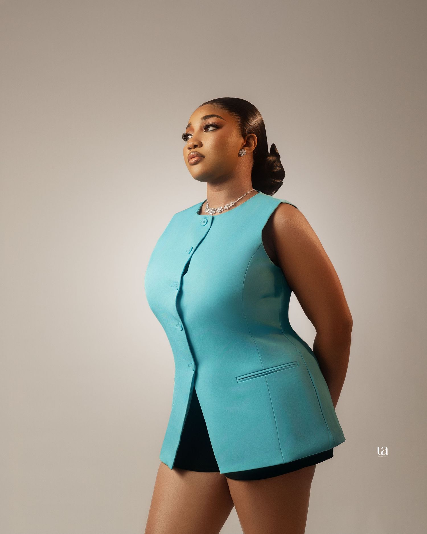 A model in a sleek turquoise cropped vest poses against a neutral backdrop in a fashion editorial series.