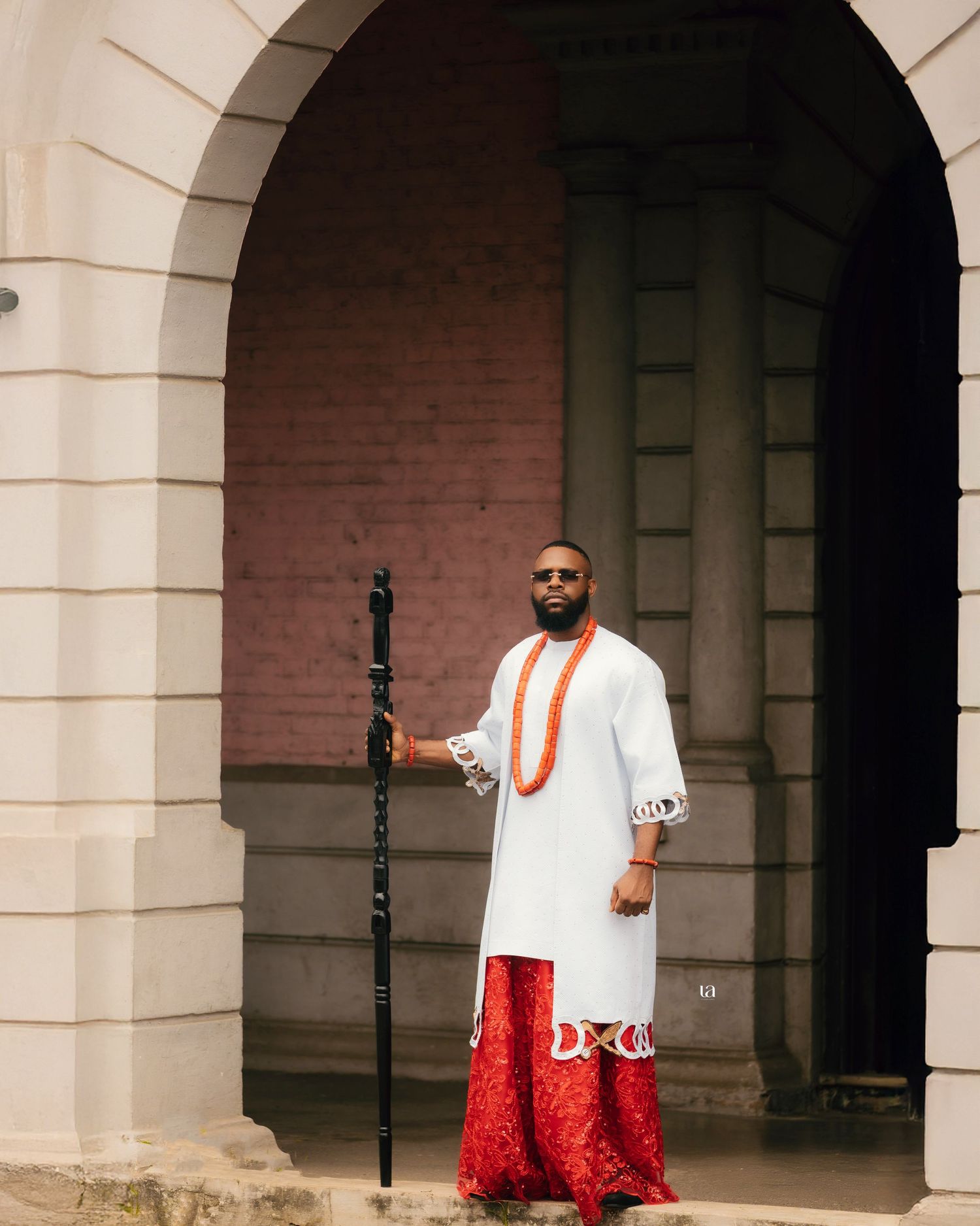 Two people in contrasting red and white outfits pose under classical stone archways.