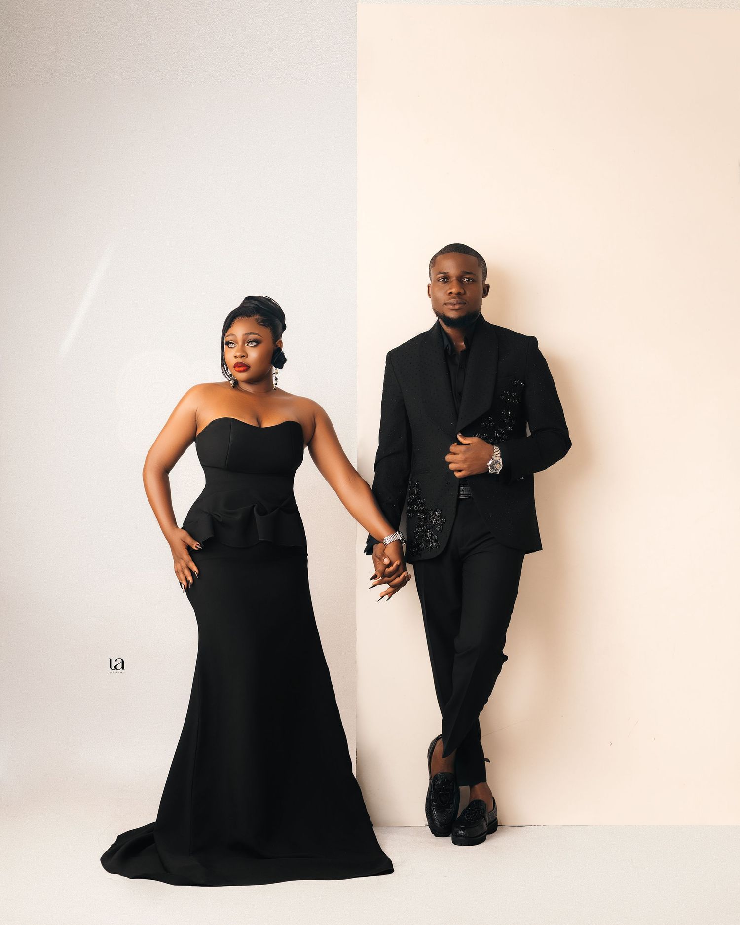 A couple poses in classic black formal wear against a white backdrop.