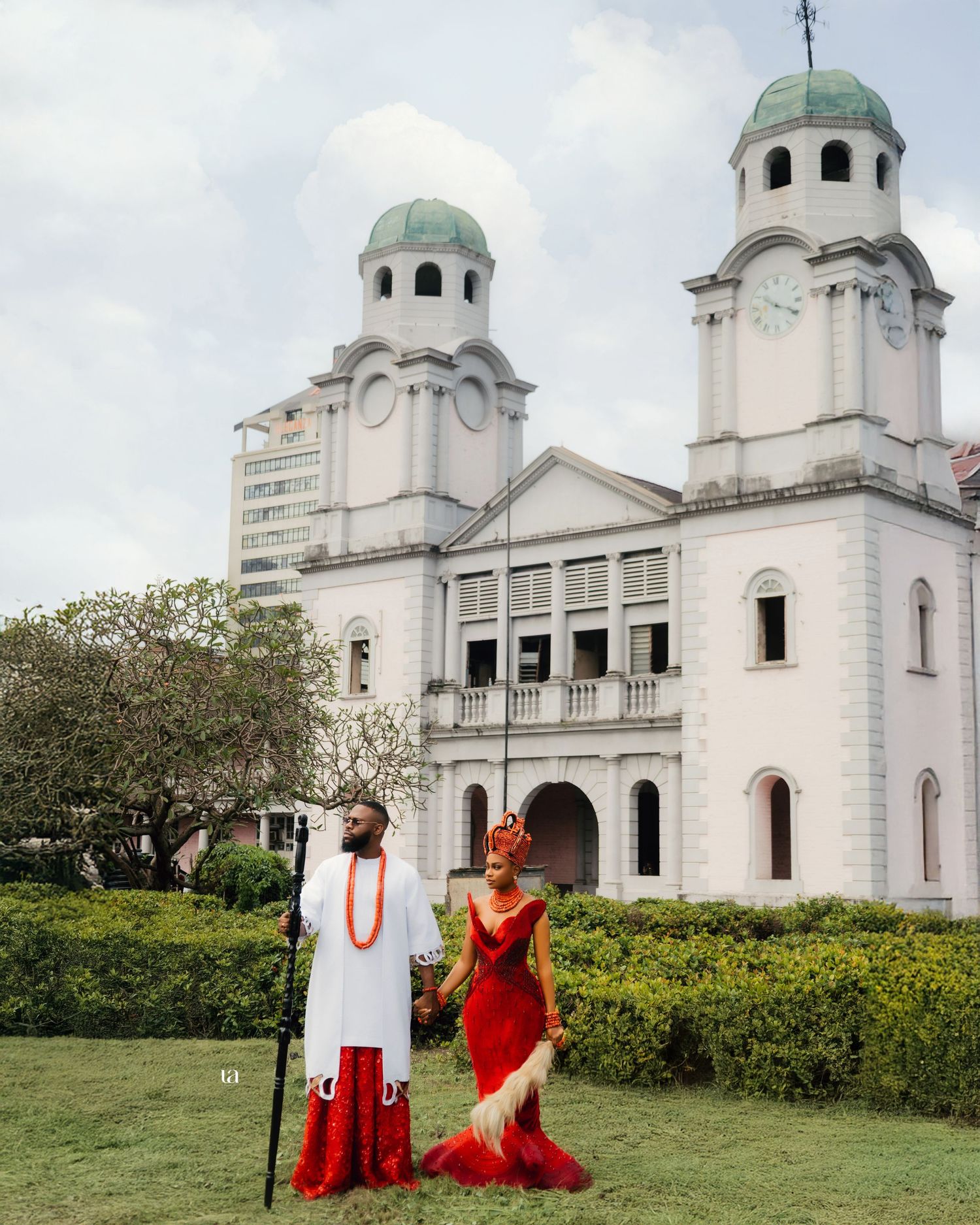 Elegant red dress photoshoot against white church architecture and garden backdrop.