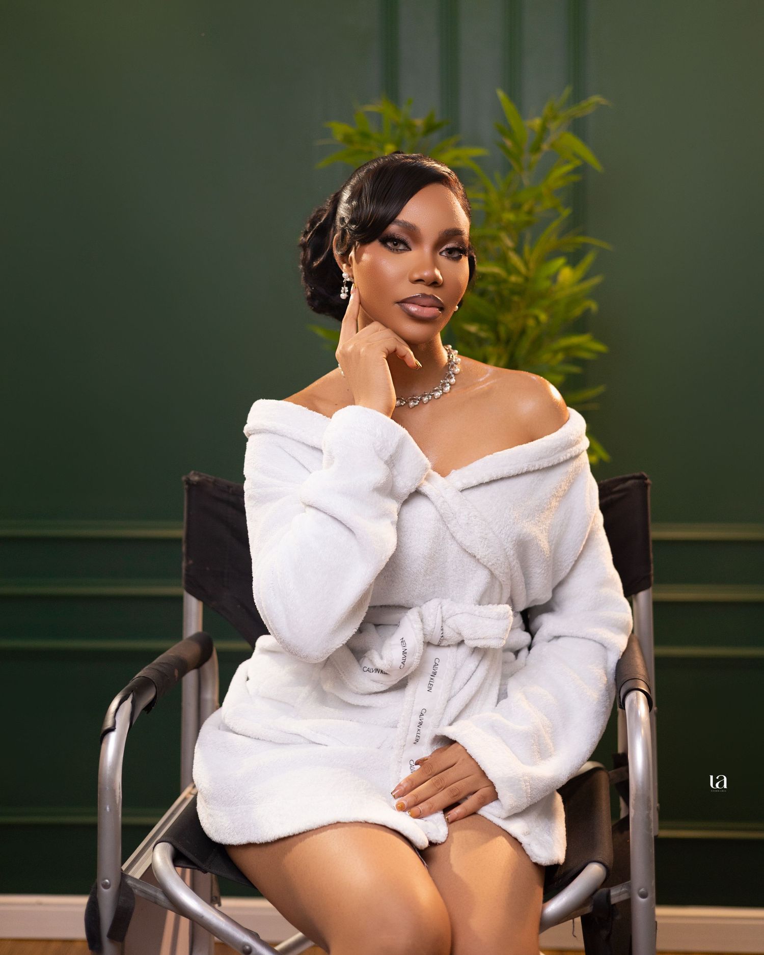 Fashion portrait in white off-shoulder outfit with elegant pose against green foliage.