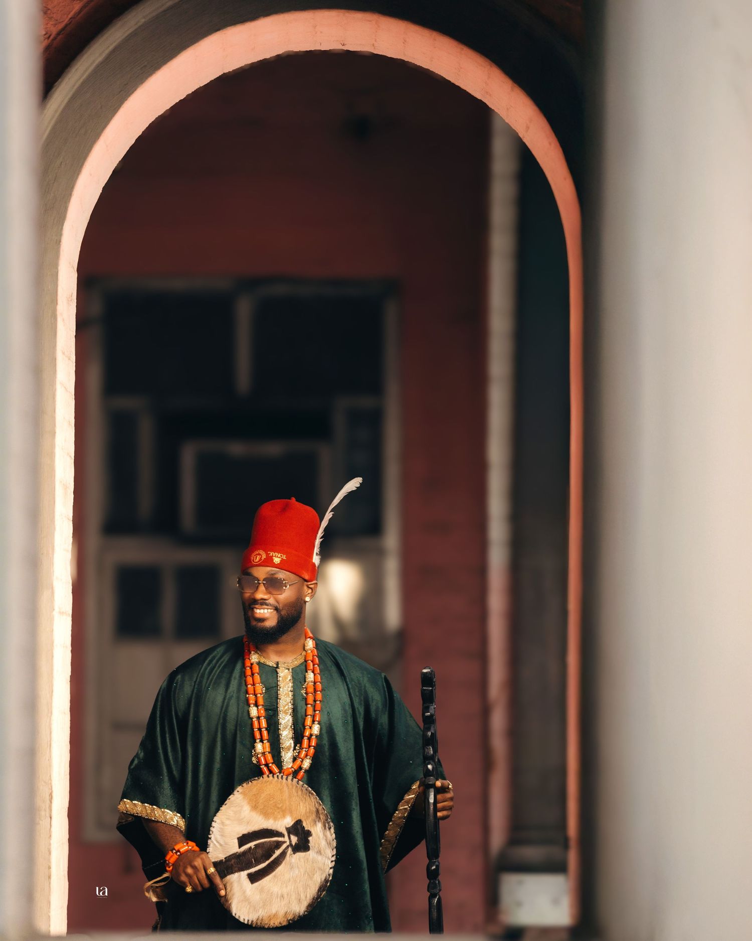 Figure in traditional African attire sits beneath ornate stone archways.
